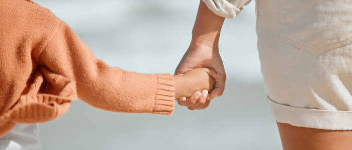 A child and mother hold hands at the beach