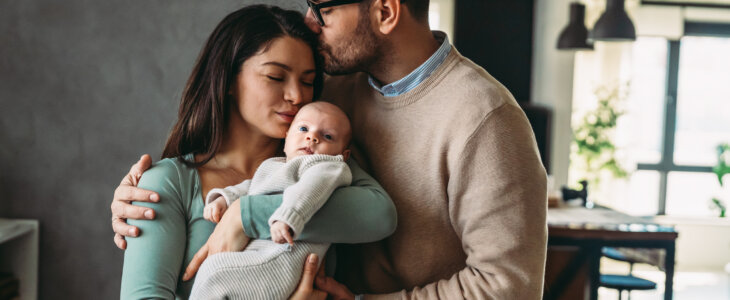 Portrait of young parents and newborn baby. Father and mother kiss and hug a beautiful newborn child. The concept of love, happy fatherhood and motherhood.
