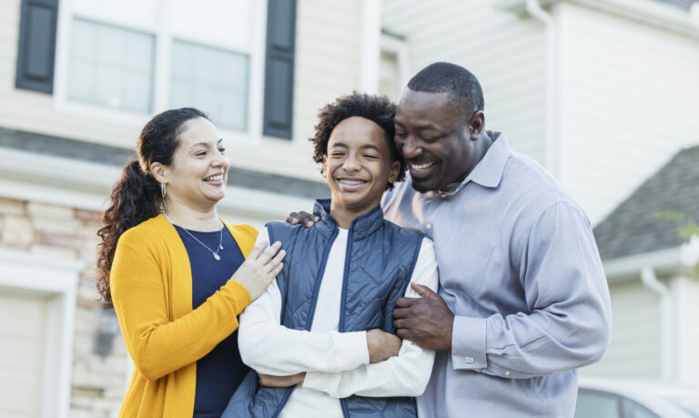 A 14 year old mixed race Hispanic and African-American teenage boy standing between his parents outside their home.