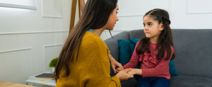 Concerned loving mother talking to her young daughter about divorce and child custody while sitting on the sofa