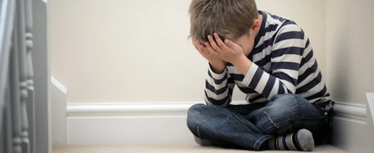 Upset problem child with head in hands sitting on staircase concept for childhood bullying, depression stress or frustration